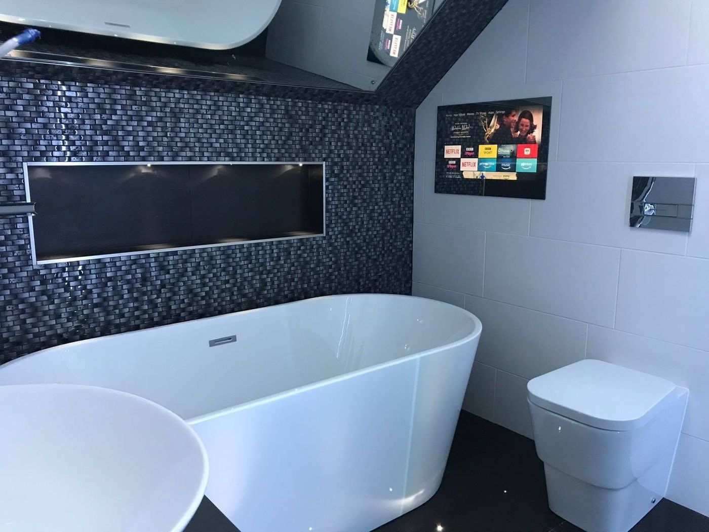 Dark feature bathroom with freestanding bath and wall-mounted TV by PJB